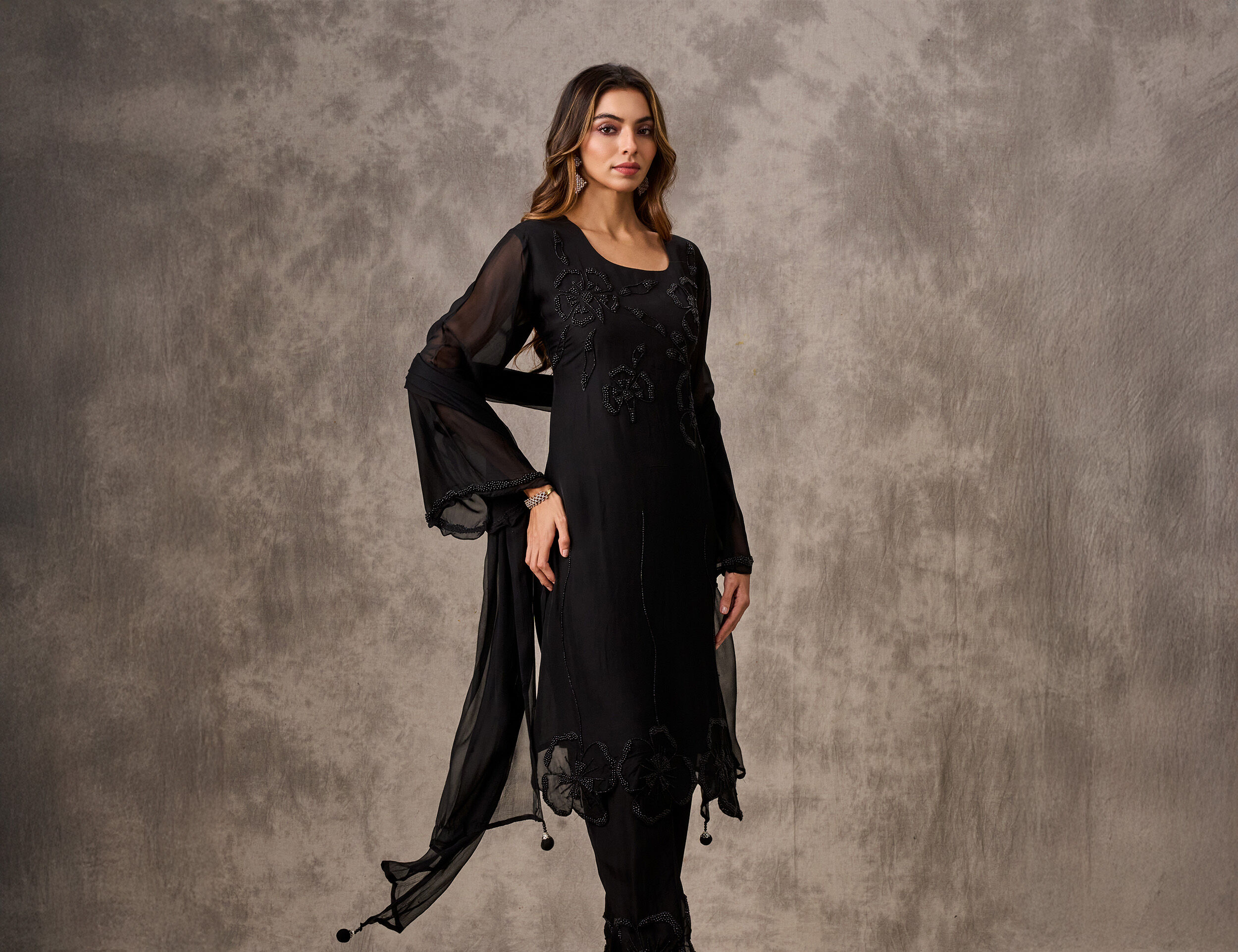 Woman in a heavily embroidered black Gharara suit with a sheer dupatta, showcasing an intricate festive outfit.
